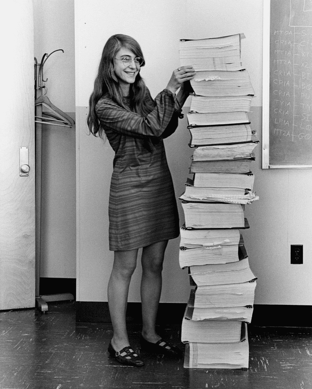 Margaret Hamilton beside the Apollo guidance software source code, printed and stacked taller than she is